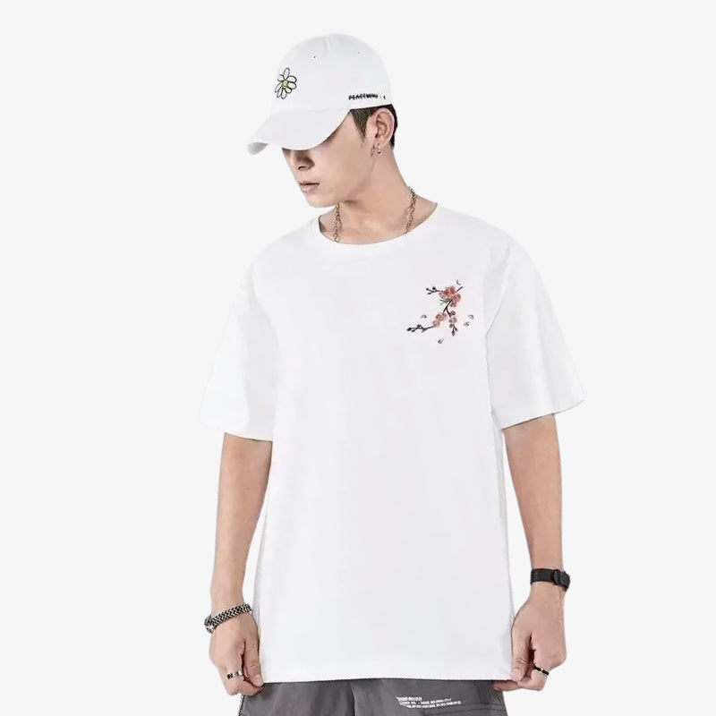 Persona con una camisa japonesa bordada para hombre y de colr blanca con diseño floral y una gorra blanca sobre fondo blanco