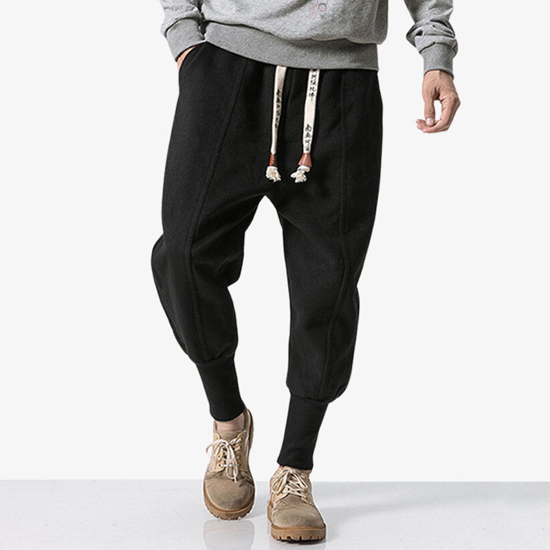 Hombre vestido con pantalones Nikka japoneses negros de estilo streetwear, con el bajo del pantalón curvado y cordones estampados con kanji