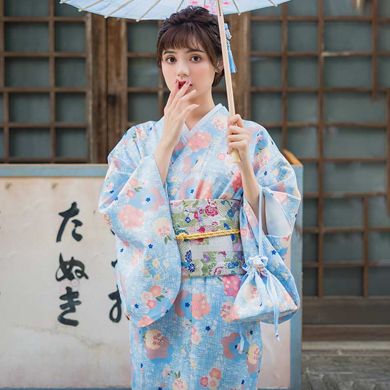 Mujer vestida con un kimono geisha floral de color azul con estampado de flores japonesas, sosteniendo un bolso a juego