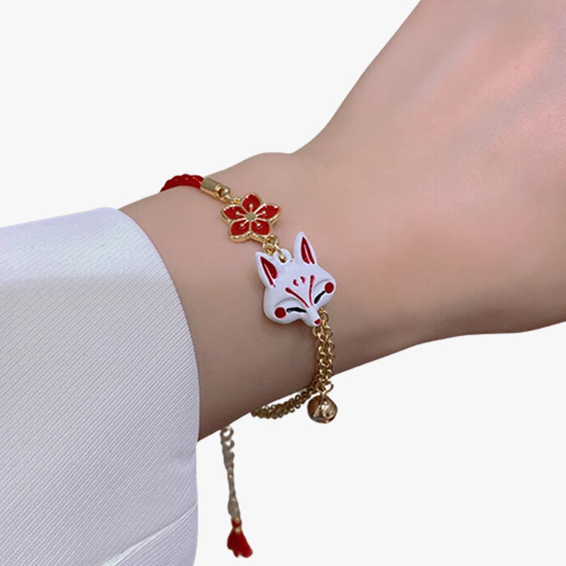 Una mujer lleva una pulsera Kitsune japonesa con cadena dorada, cabeza de zorro Kitsune y símbolo de flor de sakura en la muñeca