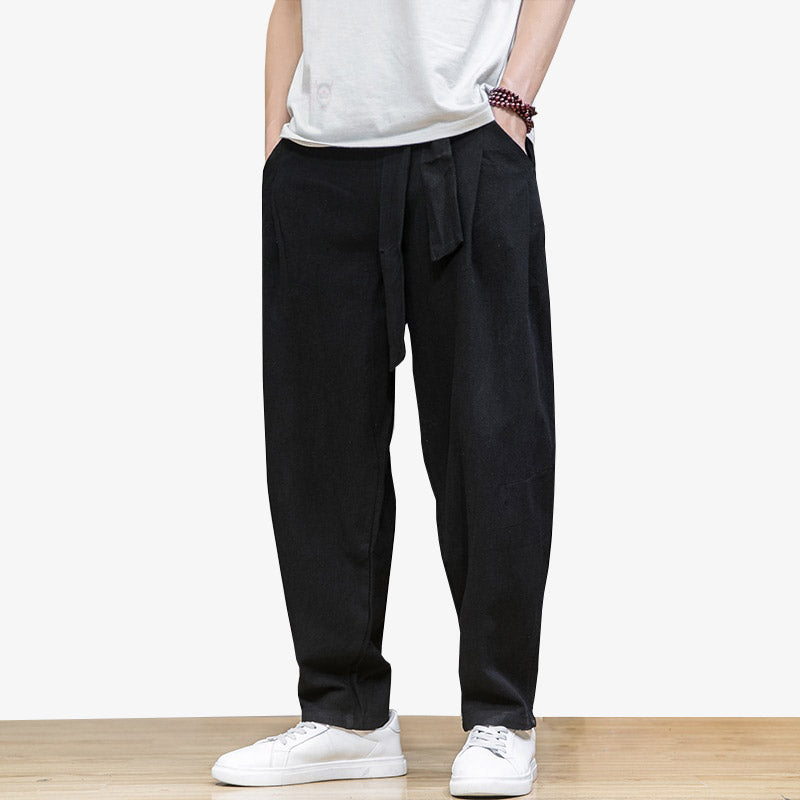 Este traje de pantalones grandes japón se abrocha con un cinturón oni. El hombre está de pie, con zapatos blancos bajos y una pulsera de perlas.