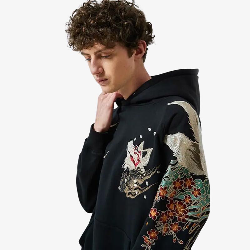 Un hombre vestido con una sudadera maison kitsune con capucha confeccionada con material de alta calidad y un elegante diseño de zorro, ideal para un look japonés moderno y mítico.