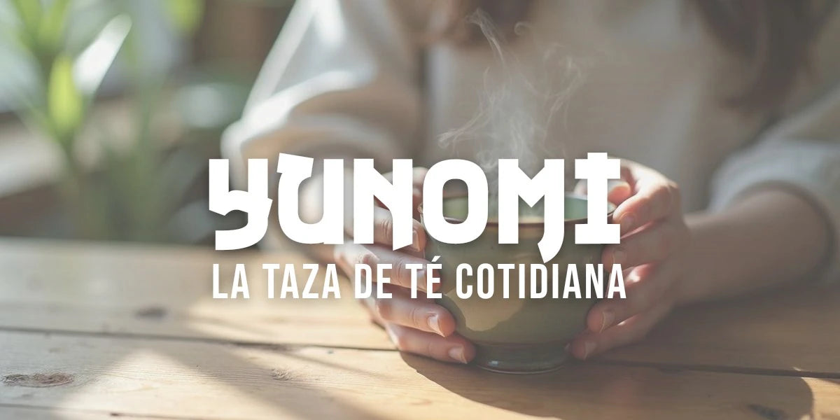 Manos sostienen un yunomi de cerámica sin asa, cilíndrico y gastado, lleno de té verde humeante sobre una mesa rústica.