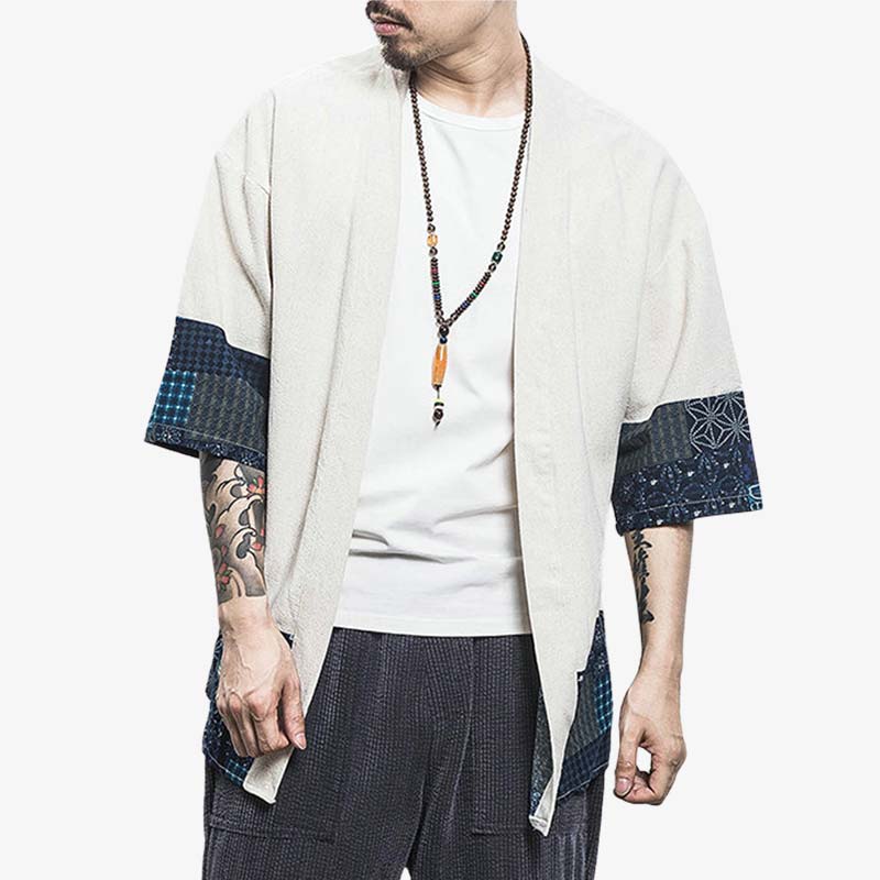 Un hombre está de pie con un Chaleco Kimono de estilo japonés. Esta prenda es una chaqueta tipo kimono que se puede llevar sobre una camiseta para conseguir un estilo japonés zen relajado. La chaqueta haori es blanca. Lleva un collar budista zen alrededor del cuello.
