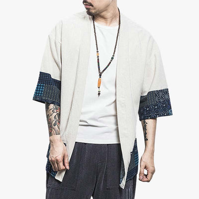 Un hombre está de pie con un Chaleco Kimono de estilo japonés. Esta prenda es una chaqueta tipo kimono que se puede llevar sobre una camiseta para conseguir un estilo japonés zen relajado. La chaqueta haori es blanca. Lleva un collar budista zen alrededor del cuello.