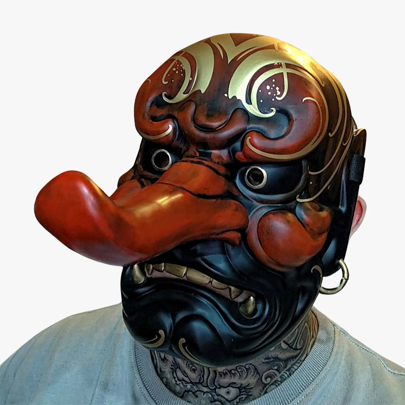 Un hombre lleva una Mascara Japonesa Tengu rojo. El material de la máscara es madera y resina de calidad. La máscara japonesa tiene una nariz larga. Es una máscara tradicional japonesa que simboliza a un demonio oni. Es una máscara de manga muy popular.