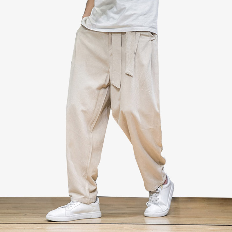 Un hombre lleva in Pantalon Japones Hombre de estilo japonés de color beige. En los pies lleva unas zapatillas deportivas blancas. Los pantalones japoneses son anchos y tienen cinturón.