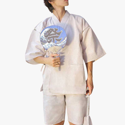 Un hombre con un Pijama Tradicional Japones de color blanco y lleva un abanico japonés uchiwa en la mano 