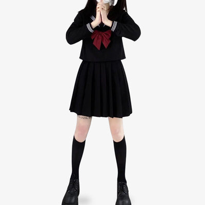 Una chica de pie vestida con un Sailor-Fuku Cosplay anime japonés de marinera. Lleva calcetines largos negros japoneses, una falda negra, un lazo rojo y una camisa escolar negra.
