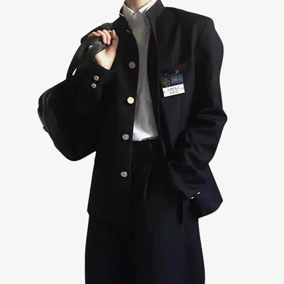 Una persona de pie viste un Uniforme Japones Hombre negro. También lleva una camisa blanca.