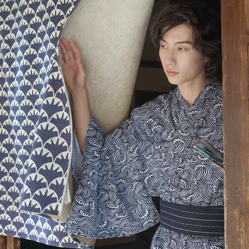 Una persona vestida con un Yukata Hombre Tradicional con estampado de olas japonesas. El kimono es de algodón. Lleva un cinturón obi oscuro atado a la cintura para cerrar el kimono masculino.