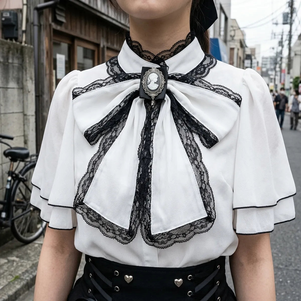 Vista de cerca del lazo negro con bordes de encaje, el camafeo de plata y el cuello capa de la blusa
