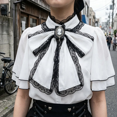 Vista de cerca del lazo negro con bordes de encaje, el camafeo de plata y el cuello capa de la blusa
