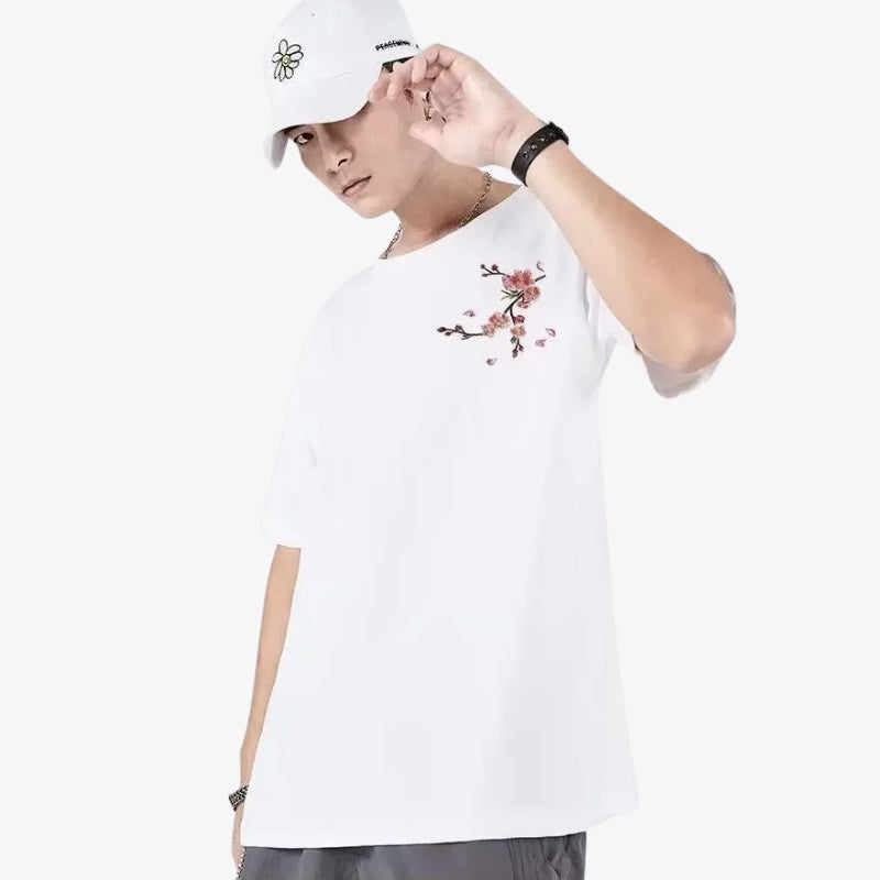 Persona con una camisa japonesa blanca sakura con bordados de cerezos en flor y una gorra blanca sobre un fondo blanco.
