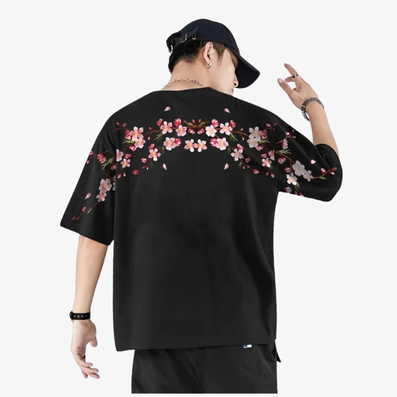 Persona con una camiseta sakura humbre de color negra de estilo urbano con diseños florales sobre fondo blanco.