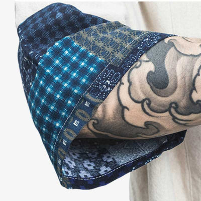 Un hombre con un tatuaje japonés en el antebrazo muestra la manga de su cardigan tipo kimono hombre de color blanco. La tela de la manga está estampada con símbolos geométricos japoneses.