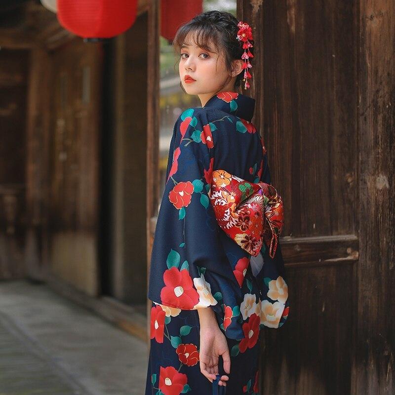 Cinturón obi para kimono japonés con flores rojas de ume sobre tela suave. La mujer lleva el kimono largo cerrado con un obi rojo y un kanzashi en el pelo