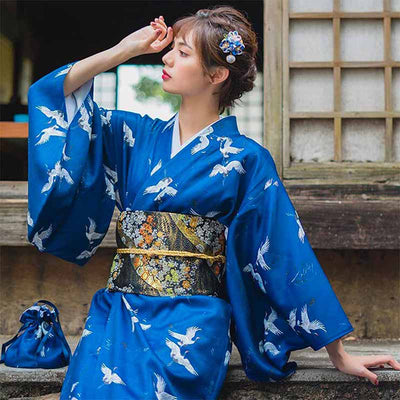 Cinturón obi floral atado a un kimono azul con grullas tsuru