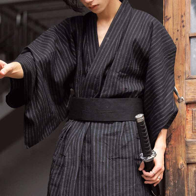 Hombre vestido con kimono negro y cinturón obi de tela negra japonesa, sosteniendo una katana