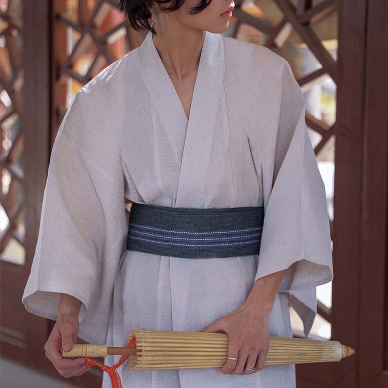 Hombre con yukata blanco y cinturón obi samurái sosteniendo una sombrilla de bambú japonesa