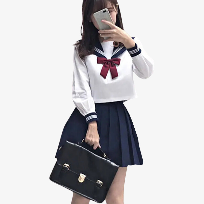 Una chica vestida con un cosplay de uniforme escolar japonés. Lleva una mochila escolar japonesa negra. Lleva una falda japonesa de color azul y una camisa escolar japonesa blanca.