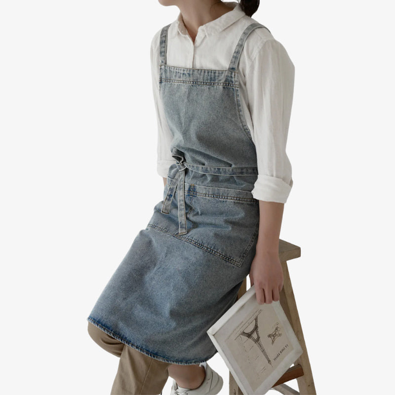 Delantal japonés de denim en algodón azul resistente, con tirantes cruzados para mayor comodidad y un práctico bolsillo frontal, perfecto para cocinar o hacer manualidades