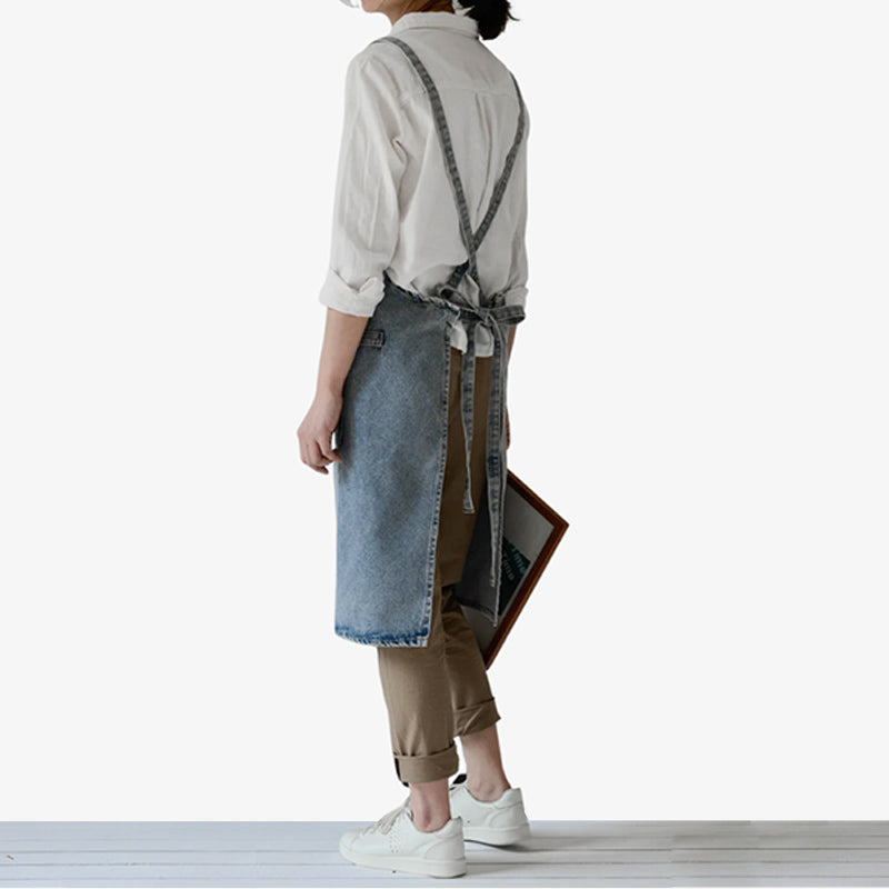 Delantal de trabajo japonés en denim azul, diseñado con tirantes cruzados y bolsillo frontal, que ofrece protección duradera y estilo para la cocina o el taller