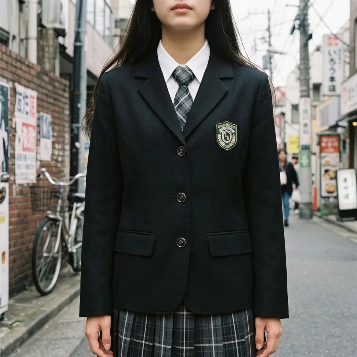 Vista cercana de la chaqueta escolar negra, el escudo bordado, el cuello blanco y la corbata de cuadros