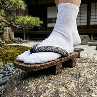 Geta con motivo seigaiha vista en ángulo de tres cuartos sobre una piedra en un jardín japonés