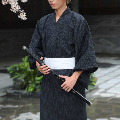 Hombre con kimono tradicional japonés cerrado con cinturón obi blanco, sosteniendo una katana negra