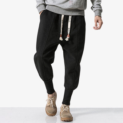 Hombre vestido con pantalones Nikka japoneses negros de estilo streetwear, con el bajo del pantalón curvado y cordones estampados con kanji