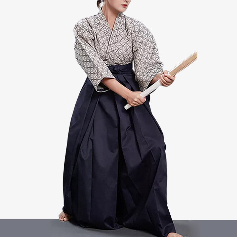 Persona practicando aikido con hakama azul marino y blanco, sosteniendo un bachi de madera