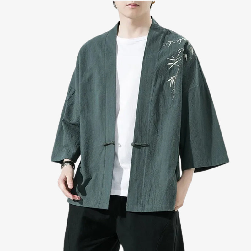 Persona con una chaqueta tipo kimono verde con bordados blancos sobre fondo blanco.