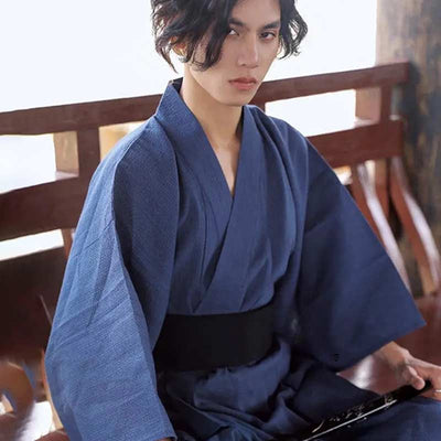 Una persona japonesa lleva un kimono japones hombre azul, la prenda tradicional japonesa, y un cinturón obi negro alrededor de la cintura.