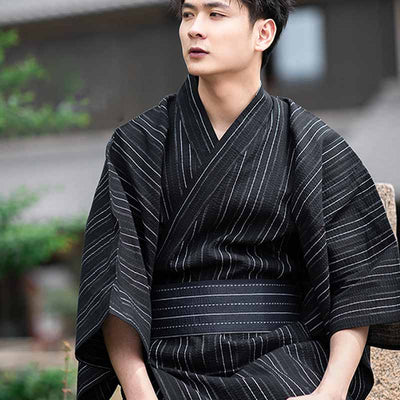 Hombre con kimono negro a rayas anudando un cinturón obi japonés