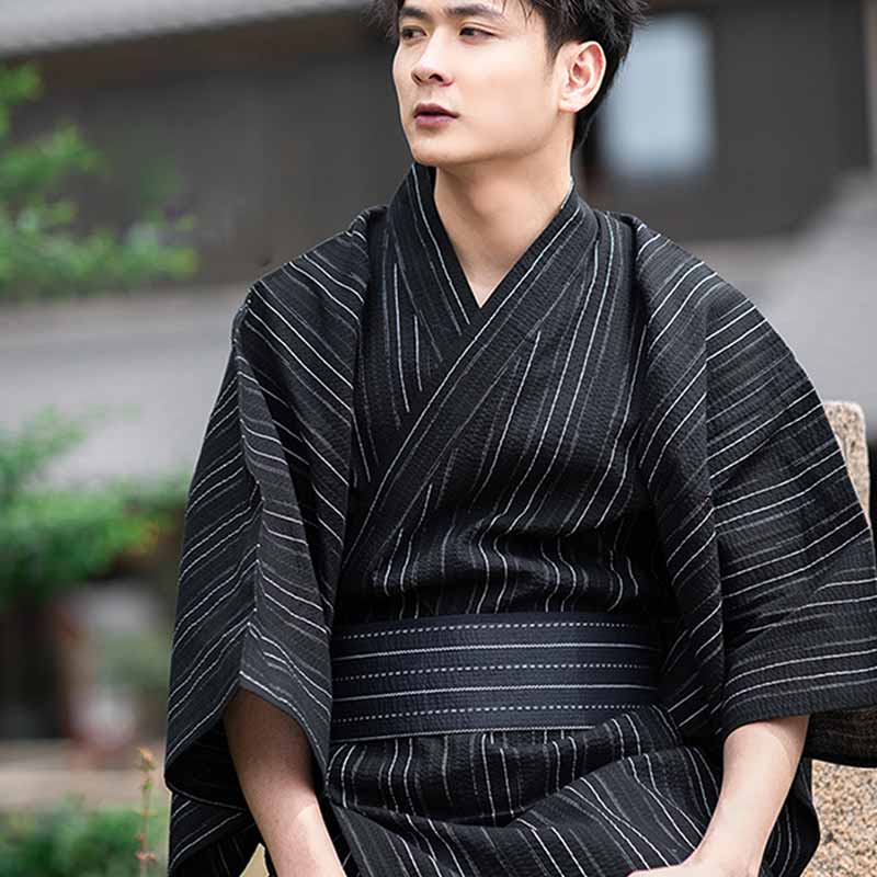 Hombre con kimono negro a rayas anudando un cinturón obi japonés