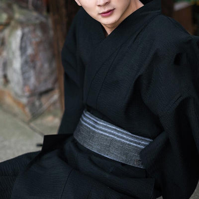Hombre asiático vestido con un kimono negro tradicional y obi gris a la cintura