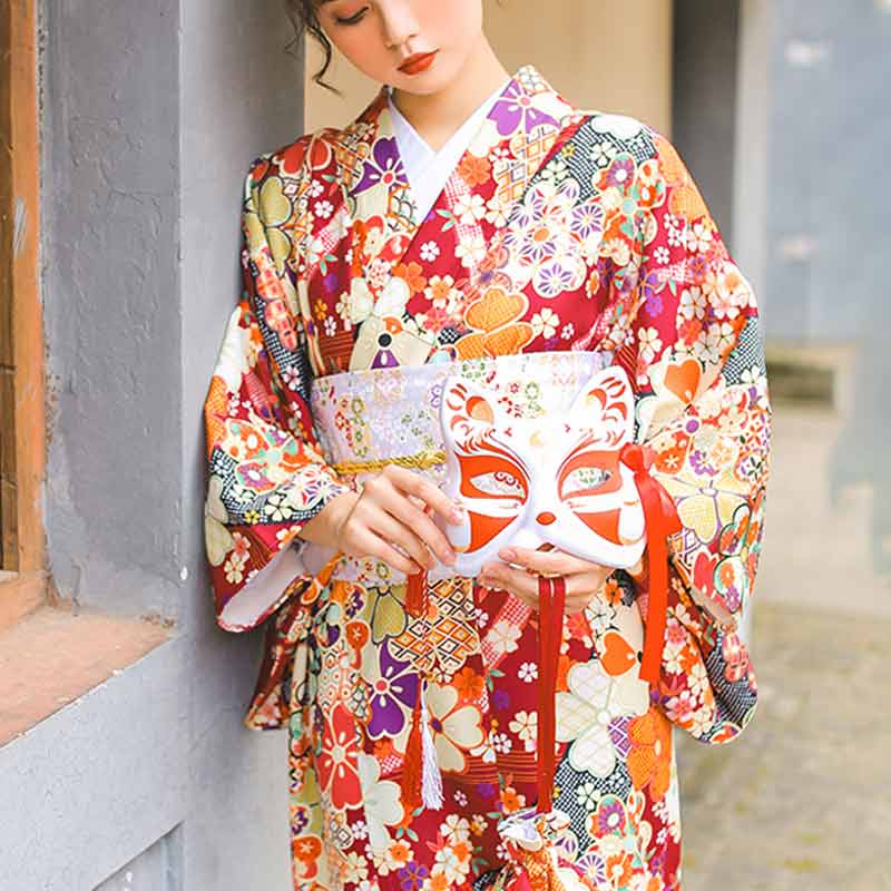 Mujer de pie con kimono estampado de sakura y máscara kitsune en las manos