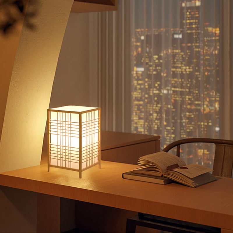 Lámpara japonesa de escritorio junto a libros con vistas a la ciudad a través de la ventana
