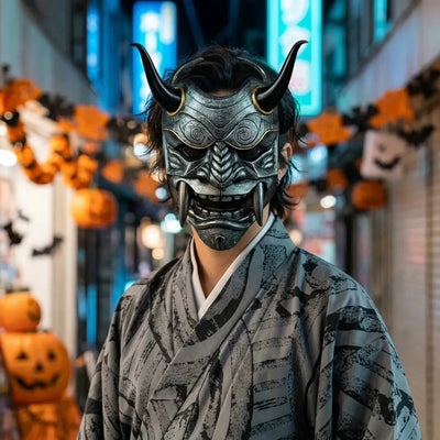 Mascara de oni: mascara de demonio metalica gris con cuernos negros, llevada con un kimono gris de noche para Halloween, con el neon azul de Tokio de fondo