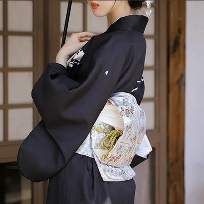Mujer luciendo un cinturón obi japonés sobre un kimono negro tradicional