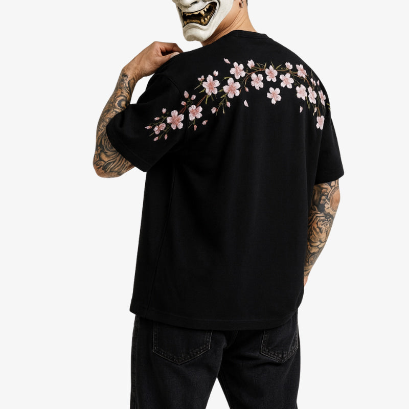 Persona con una negra camiseta Sakura con diseños florales en la espalda, de pie sobre un fondo blanco.