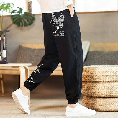 Hombre con pantalón japonés negro estampado de grullas blancas, combinado con camisa blanca y zapatillas blancas, en una habitación de suelo de madera