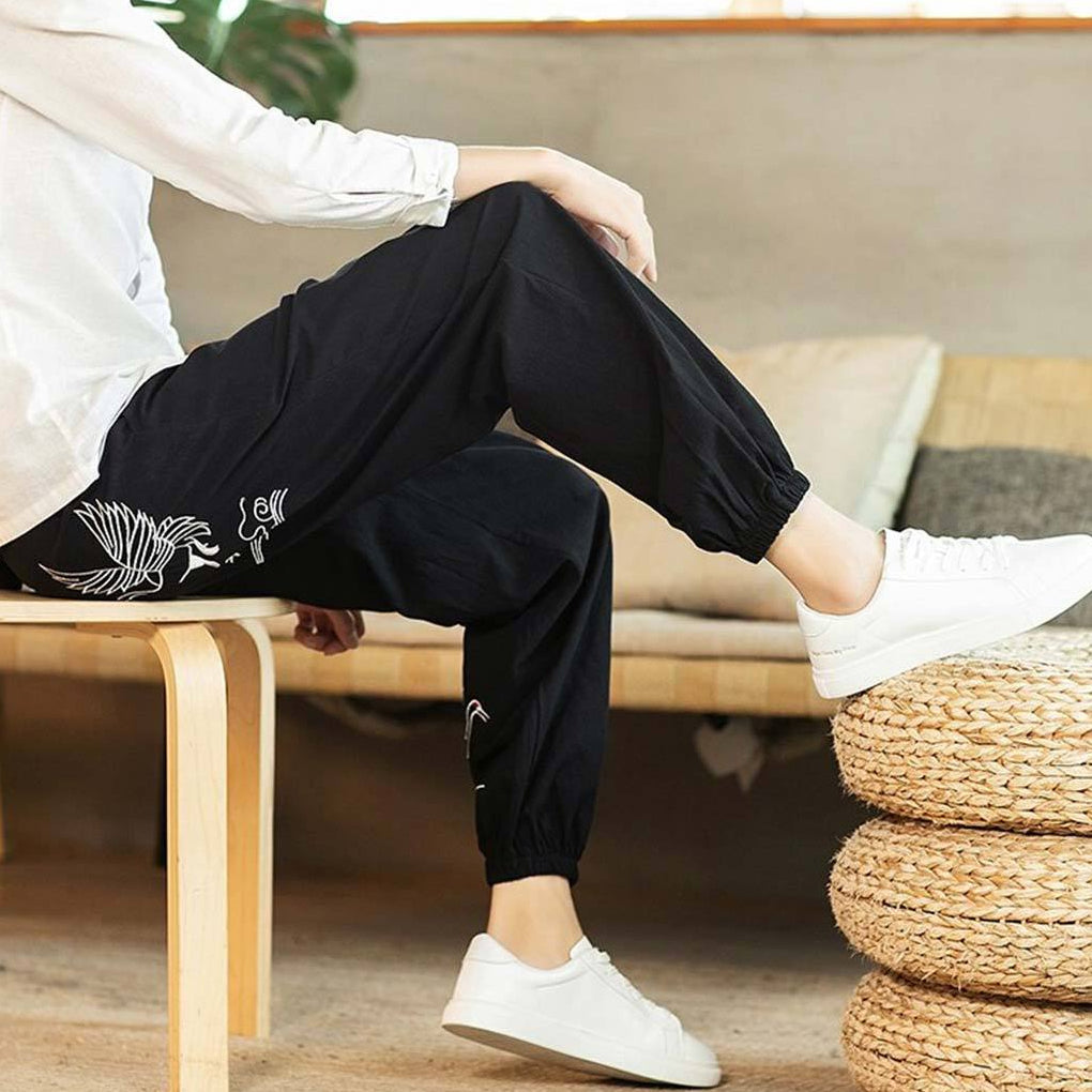 Persona sentada en un taburete de madera con pantalón japonés zen de grullas y diseños blancos