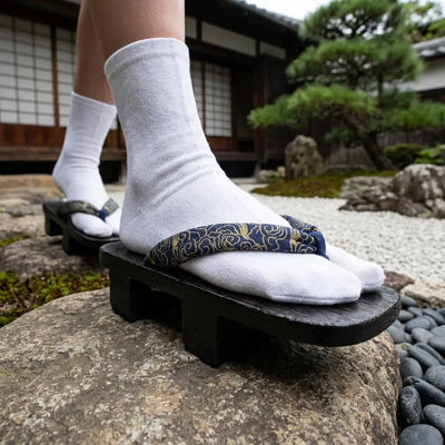 Sandalias Geta Karakusa con correas hanao azules sobre una piedra en un jardín japonés