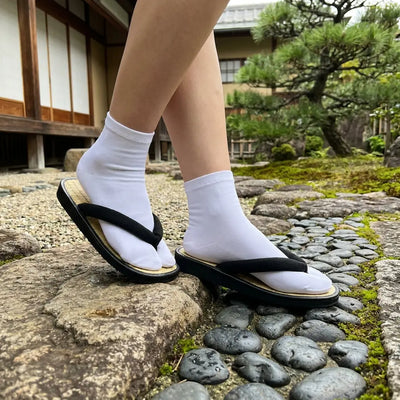 Sandalias geta de paja trenzada con tira negra sobre piedra de jardín japonés