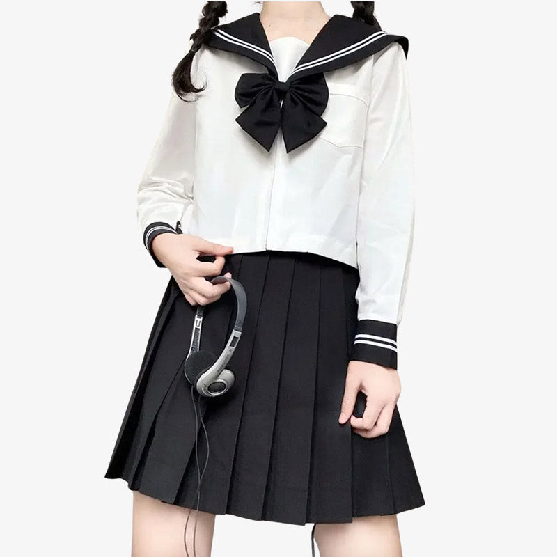 Una mujer de pie vestida con un uniforme sailor fuku japonés de colegiala. Lleva una falda japonesa negra, una camisa japonesa blanca de manga larga y un lazo negro con rayas blancas.