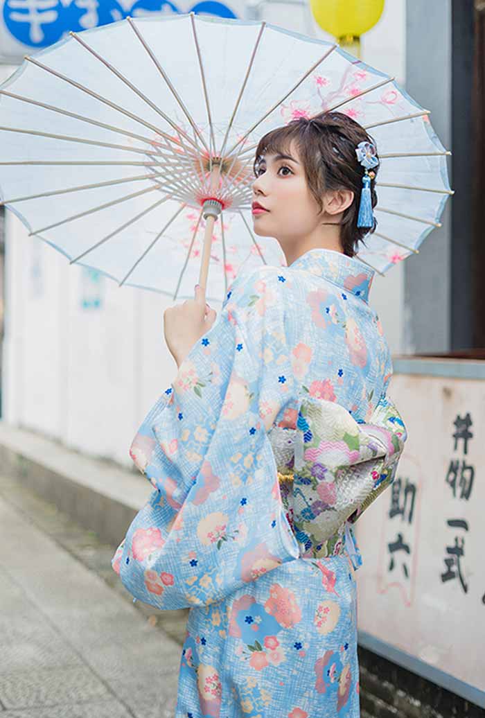 Yukata mujer con flores en tonos suaves, la mujer sostiene un wagasa que realza la elegancia del conjunto